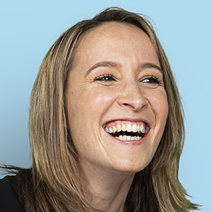 Nahaufnahme einer lachenden Frau mit offenen Haaren vor einem hellblauen Hintergrund.