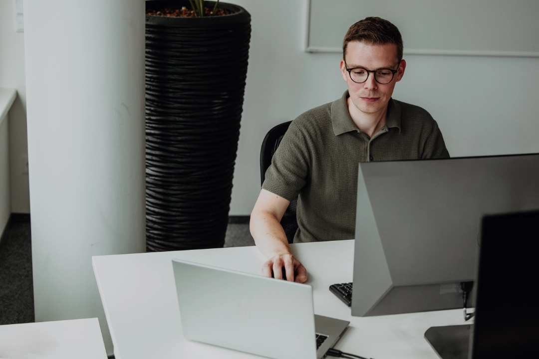 Un collaborateur expérimenté travaille de manière concentrée sur un ordinateur portable et un écran dans un bureau moderne – autonomie, expertise professionnelle et perspectives de développement attractives chez BSI Software.