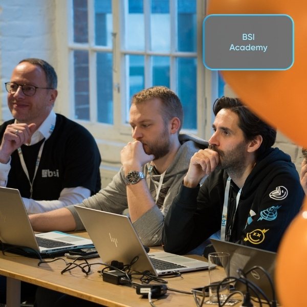 Des participants de la BSI Academy travaillent concentrés sur leurs ordinateurs portables lors du BSI Campus 2025 ; un bouton gris clair "BSI Academy" est visible en haut à droite.