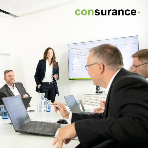 Meeting in a modern conference room with multiple people and laptops; presentation on a large screen – consurance, a partner of BSI Software.