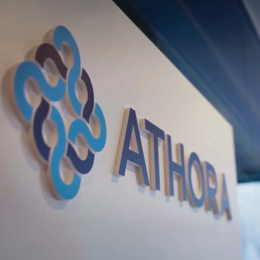 Close-up of the blue and turquoise Athora logo mounted on a bright office wall. Athora is a BSI Software customer and uses solutions for digital customer relationship management and the creation of compelling customer experiences.