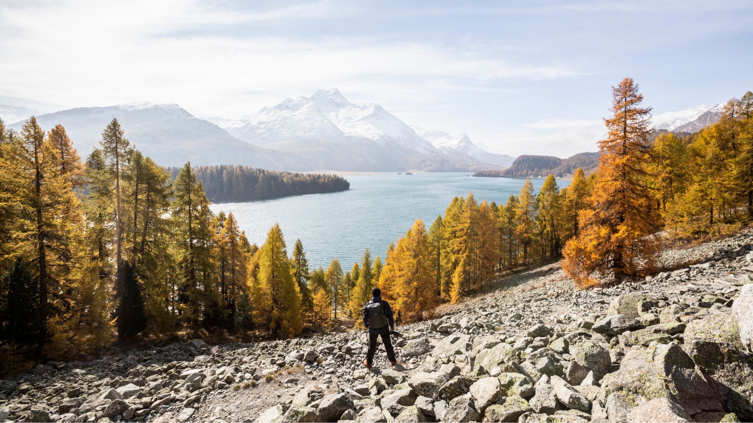 Urs Frick von BSI Software beim Wandern in herbstlicher Berglandschaft mit Blick auf den Silsersee im Engadin, eine Kamera in der Hand haltend.