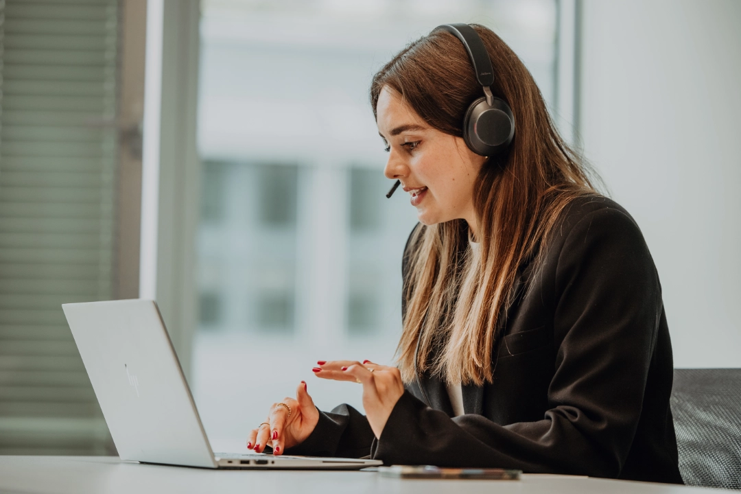 Une stagiaire ou étudiante en emploi travaille sur un ordinateur portable avec un casque et participe à un échange virtuel – modèles de travail flexibles, développement personnel et expérience pratique chez BSI Software.