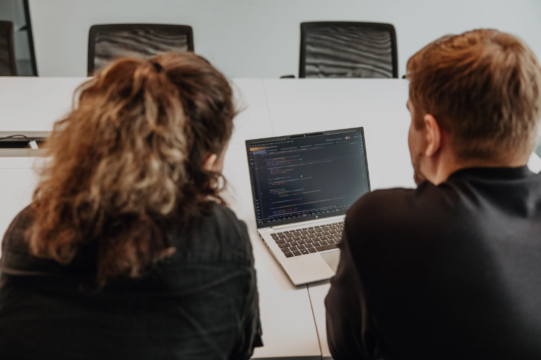 Deux collaborateurs travaillent ensemble sur un ordinateur portable et analysent du code – formation pratique, encadrement étroit et aperçu du développement logiciel durant un apprentissage chez BSI Software en Suisse.