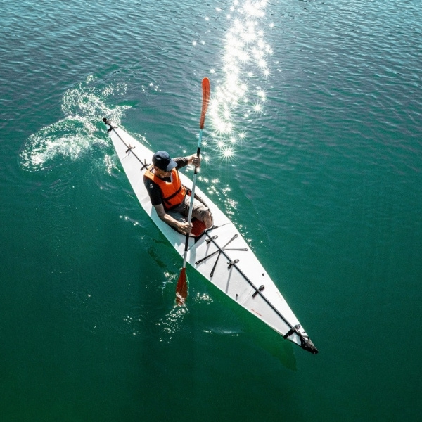 Thomas Lindauer mit Rettungsweste paddelt in einem weissen Kajak über türkisfarbenes Wasser, umgeben von Sonnenreflexen auf der Wasseroberfläche.