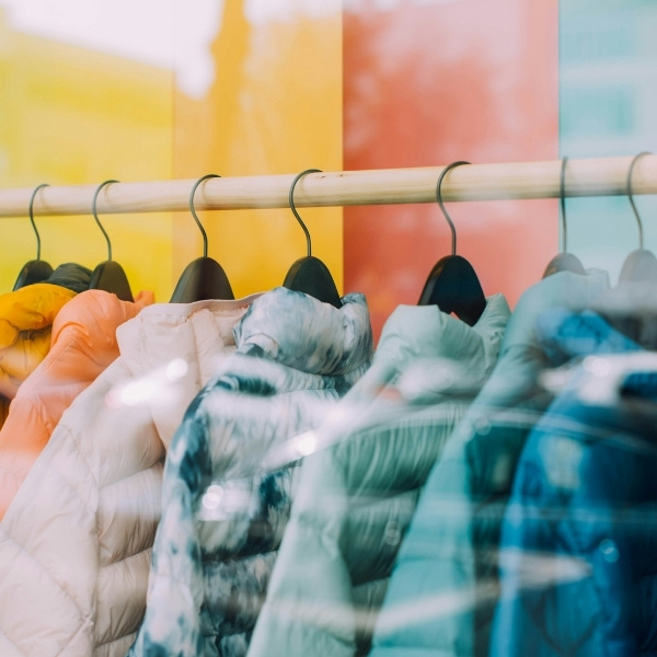 View through a shop window showing a clothing rack with colorful winter jackets – symbolic image for customer data management in retail with the BSI Customer Suite