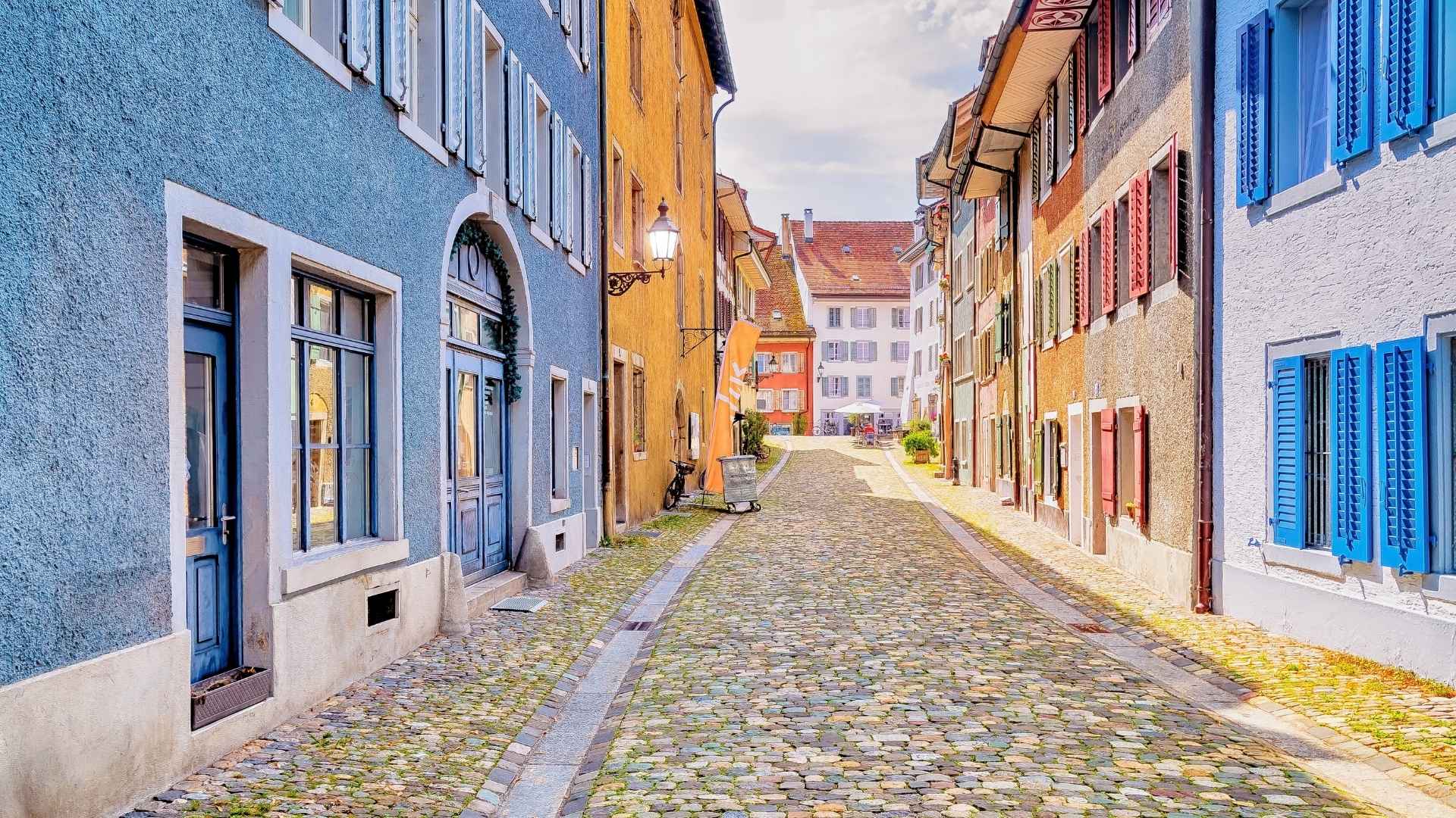 Historische Altstadtgasse in Baden mit Kopfsteinpflaster, farbigen Fassaden und Fensterläden typischer Schweizer Stadthäuser. In Baden befindet sich der älteste Standort von BSI Software. Hier wurde das Unternehmen 1996 gegründet.